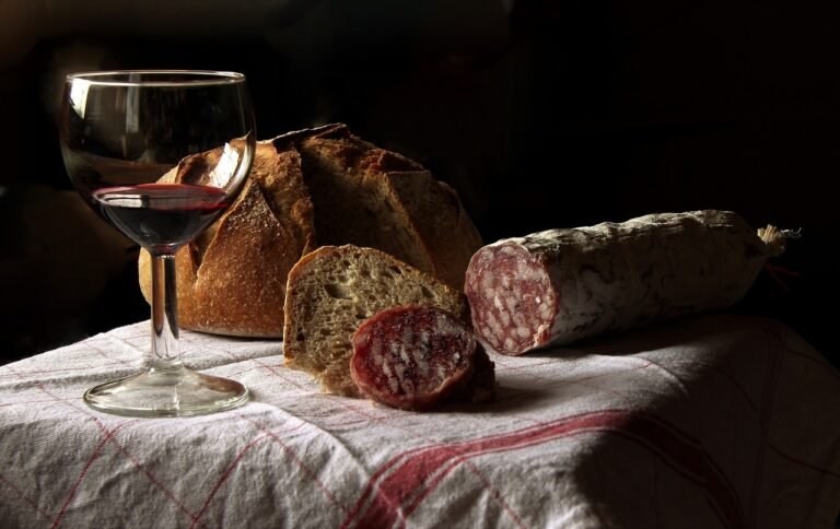 Close up photo of a glass of wine, a loaf of bread and sausage chub